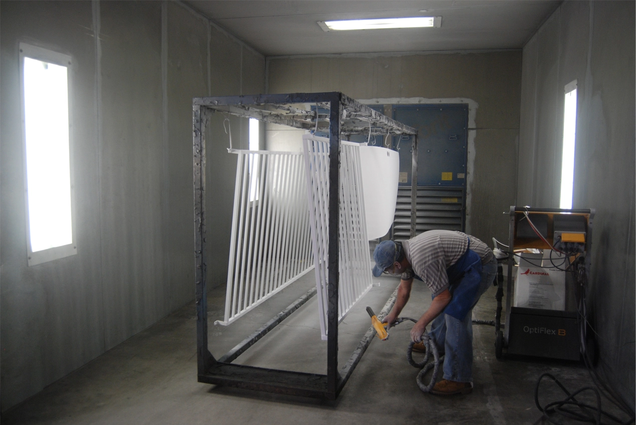Technician powder-coating metal railing panels inside a finishing booth