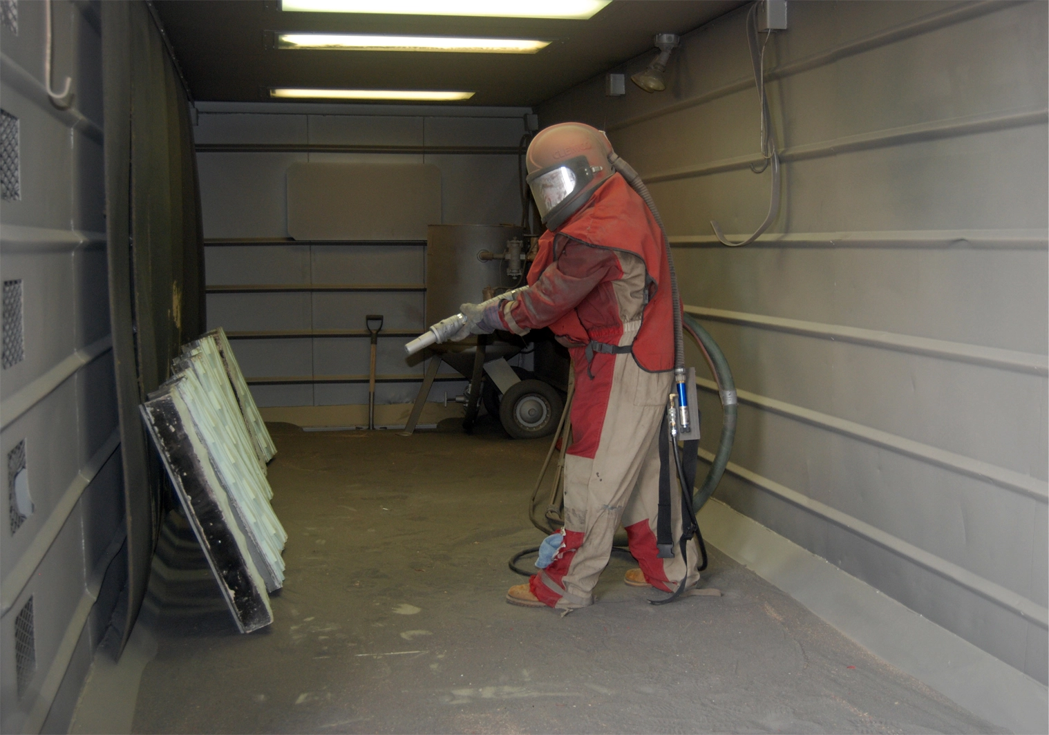 Technician sandblasting metal panels inside a blast booth